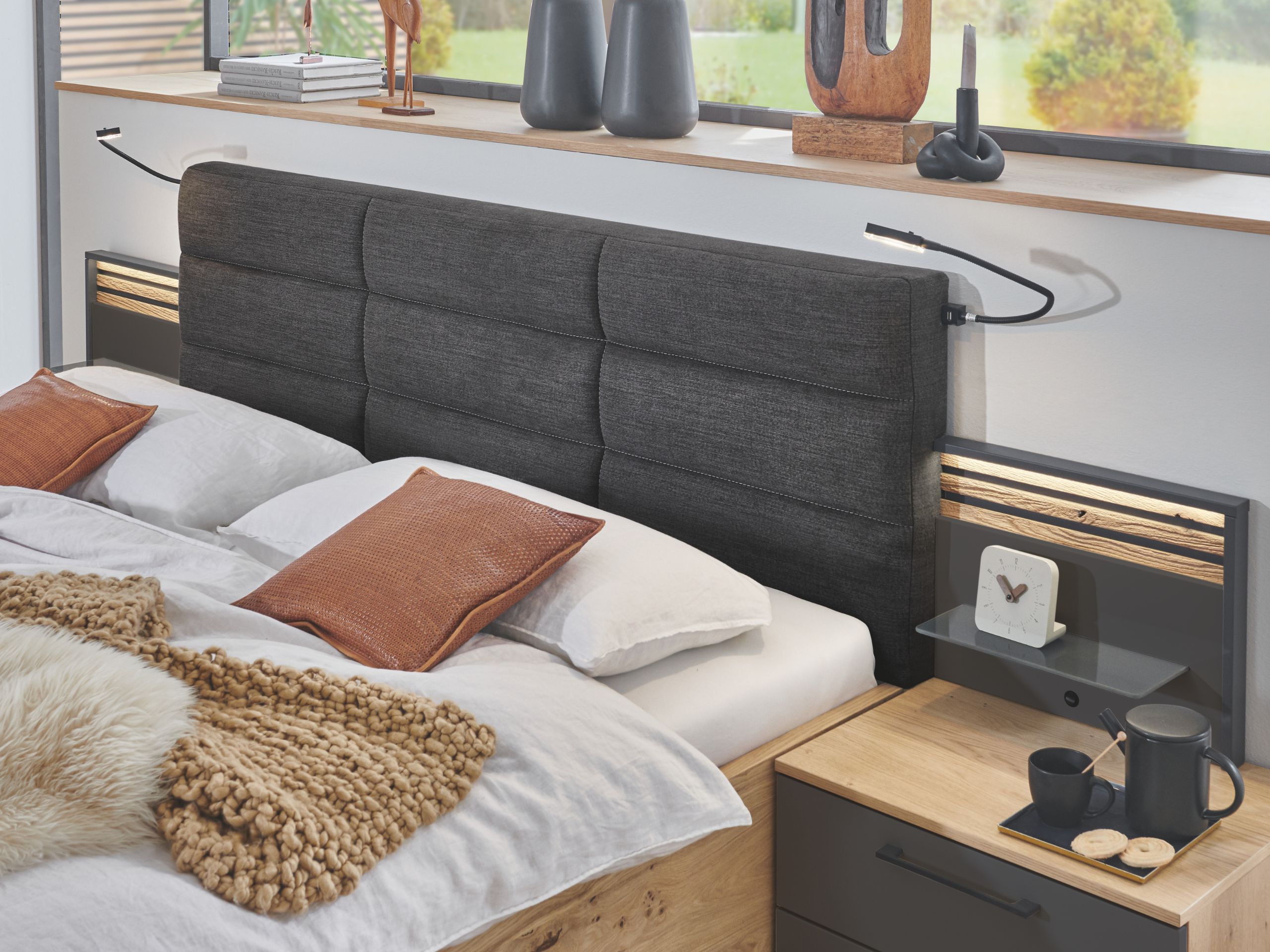 Disselkamp Cabrillo Zubehor Millieu_Ausschnitt Bett mit Polsterkopfteil, Nachtischkonsole mit Panelaufsatz in Lack Basalt und Balkeneiche und Beleuchtung