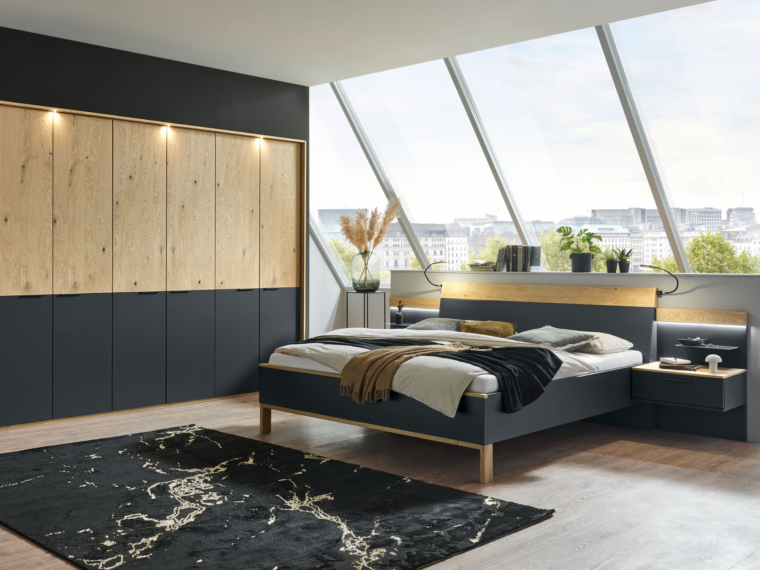 Schlafzimmerkombination Cineo mit sechstürigem Kleiderschrank, Doppelbett mit Winkelfüßen und Hängekonsolen mit Panelaufsatz und Glasboden, sowie indirekter Beleuchtung.